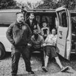 home photo of band sitting in front of van